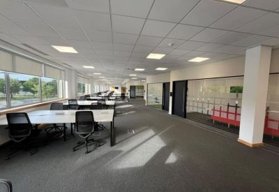 Spacious open-plan workspace with rows of white desks and ergonomic black chairs.
