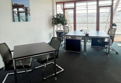 Bright corner office with two workstations and a small meeting table by a large window.