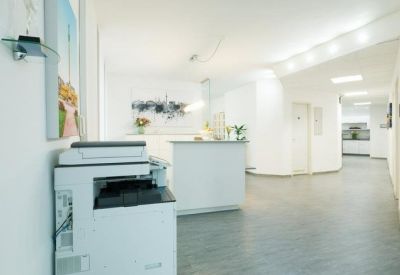 Bright, white reception area with a modern desk and a professional printer in the foreground.