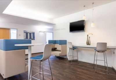 Modern breakroom area with high chairs, a wall-mounted TV, and acoustic booths.