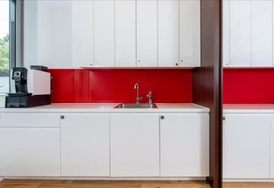 Clean kitchen area featuring white cabinetry and a bold red backsplash.
