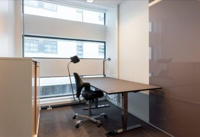Private office suite with a height-adjustable desk and floor lamp by a window.