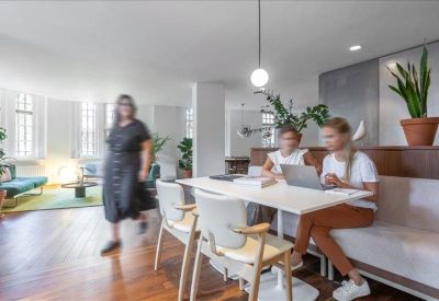 Bright communal dining and work area with wooden floors and contemporary white chairs.