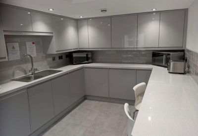 Sleek U-shaped communal kitchen with grey gloss cabinetry and white countertops.