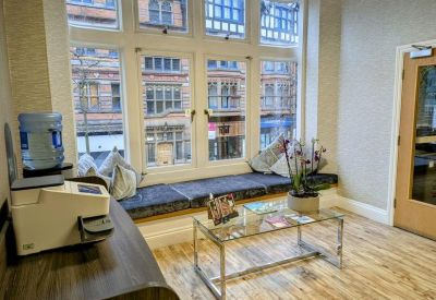 Bright reception waiting area with a glass coffee table and large windows overlooking the street.