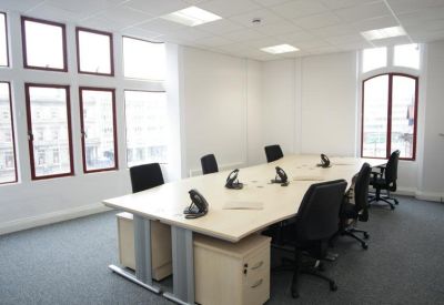 Spacious open-plan office with multiple desks, black chairs, and large windows.