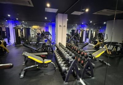 Modern gym facility with weight benches, dumbbell racks, and blue accent lighting.