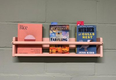 Small pink wall shelf holding three colorful books.