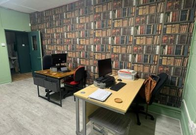 Office workspace featuring a large bookshelf-patterned wallpaper and wooden desks.