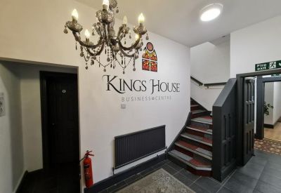 Entrance lobby with a decorative chandelier, branded signage, and a staircase with dark wood accents.