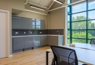 Modern communal kitchen area with grey cabinetry and a large window overlooking trees.