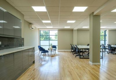 Open-plan office space featuring light wood floors, communal desks, and a lounge area.