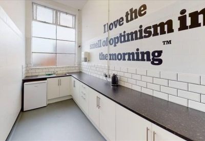Modern kitchenette with white cabinetry, dark countertops, and motivational wall graphics.