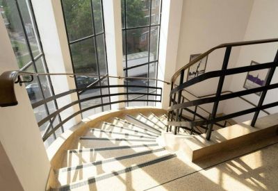 Spiral staircase with black railings situated next to a floor-to-ceiling glass wall.