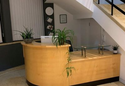 Reception area with a curved wooden desk located beneath an architectural staircase.