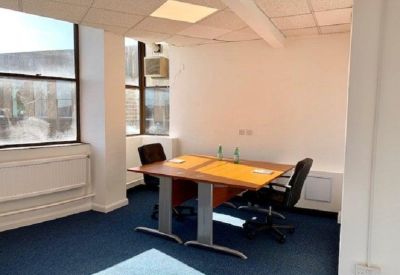 Simple meeting room setup with two desks and chairs under bright fluorescent lighting.
