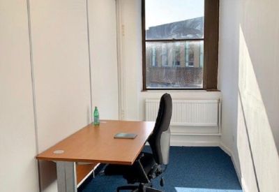 Narrow private workspace with a desk, black chair, and blue carpeting.