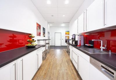 Sleek office kitchen with white cabinetry, dark countertops, and a bold red backsplash.