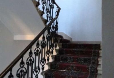 Grand internal staircase with a red patterned carpet runner and black metal banister.