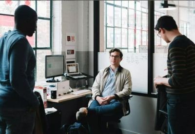 Informal meeting area with people standing and talking near a desk and computer.