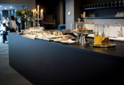 Black stone communal kitchen counter with breakfast catering and glassware.
