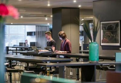 Open-plan office space featuring long dark workstations and ergonomic chairs.