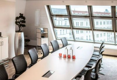 Bright conference room with a large oval table and city views through slanted windows.