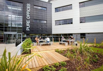 Outdoor wooden decking area with picnic tables and greenery.