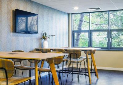 Casual breakout area with high wooden tables, yellow-legged chairs, and large windows.