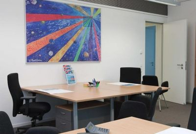 Four-person office suite featuring a large wooden desk and vibrant abstract wall art.
