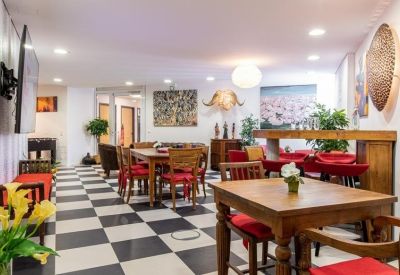 Spacious communal lounge with checkered flooring, wooden tables, and red chairs.