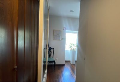 Bright hallway with wood flooring leading to a reception area with a decorative chair.