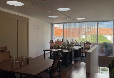 Spacious sunlit office with multiple wooden desks and view of red-tiled roofs.