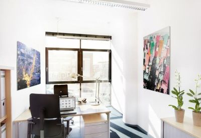 Private office suite featuring a dark ergonomic chair, light wood desk, and abstract wall art.