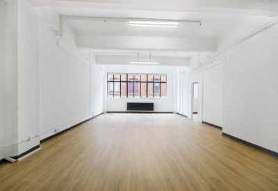 Light-filled workspace featuring blonde wood-style flooring and large industrial windows.