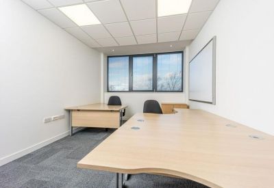 Minimalist two-person office suite with light wood desks and large windows.