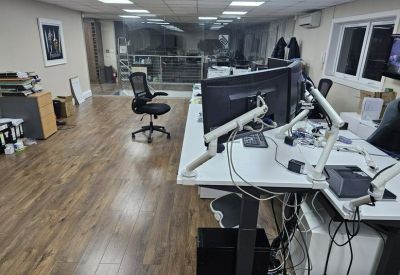 Open-plan office workspace featuring multiple monitor setups on white desks and wood-style flooring.