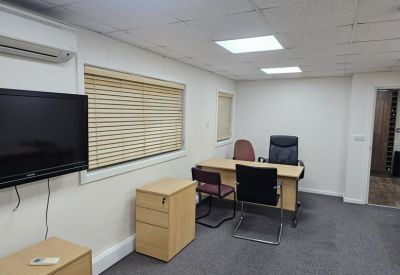 Private office suite with a wooden desk, multiple chairs, and a wall-mounted screen.