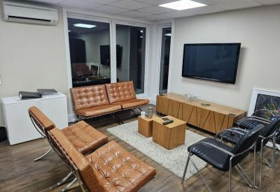 Communal lounge area with tan leather chairs, wooden coffee tables, and a large television.