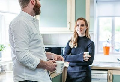 Communal kitchen area with people chatting and drinking coffee.