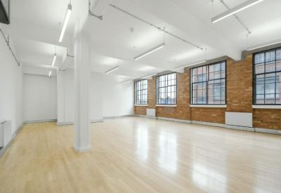 Bright, empty open-plan office with polished wood floors and exposed brick walls.