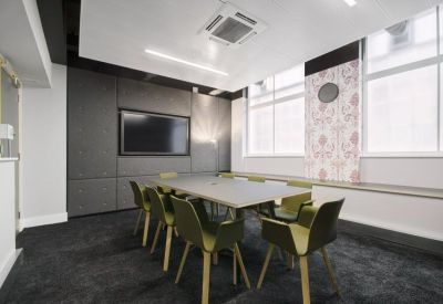 Modern meeting room with a dark carpet, grey feature wall, and green armchairs.