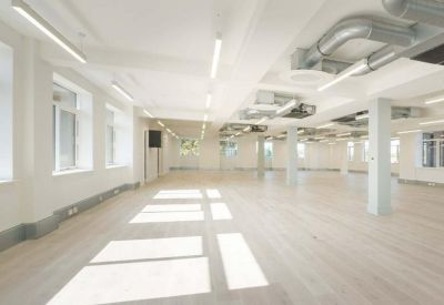 Spacious open-plan office with white walls, light wood flooring, and exposed ductwork.