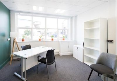 Bright private office with white desk, black chairs, and dark green feature wall.