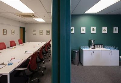 Split view of a boardroom with red chairs and a coffee station against a green wall.