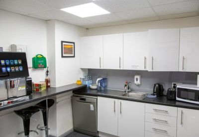 Modern communal kitchen with white cabinetry, a coffee station, and a breakfast bar with stools.