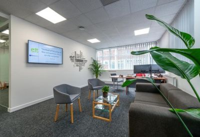 Reception lounge area with comfortable grey seating, a glass coffee table, and indoor greenery.