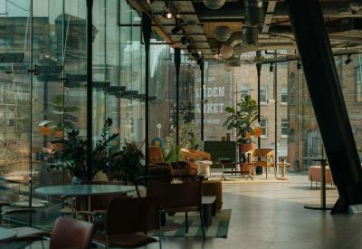 Bright communal lounge with cafe seating, indoor plants, and views of the surrounding area.