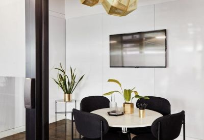 Small modern meeting room with a round table, four black chairs, and a wall-mounted screen.