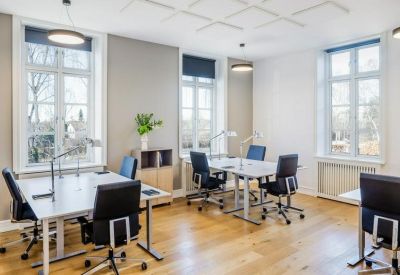Bright open-plan office with white desks and large windows overlooking trees.